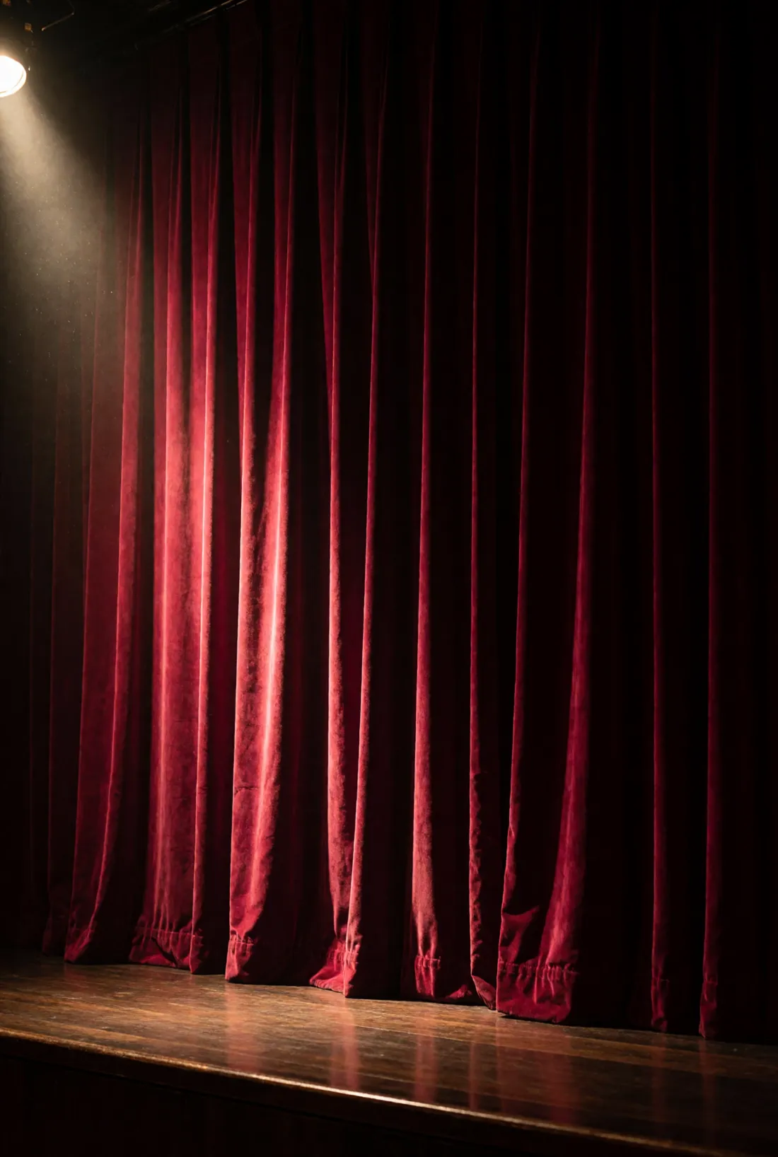 A deep crimson velvet stage curtain in an empty club, lit from one side